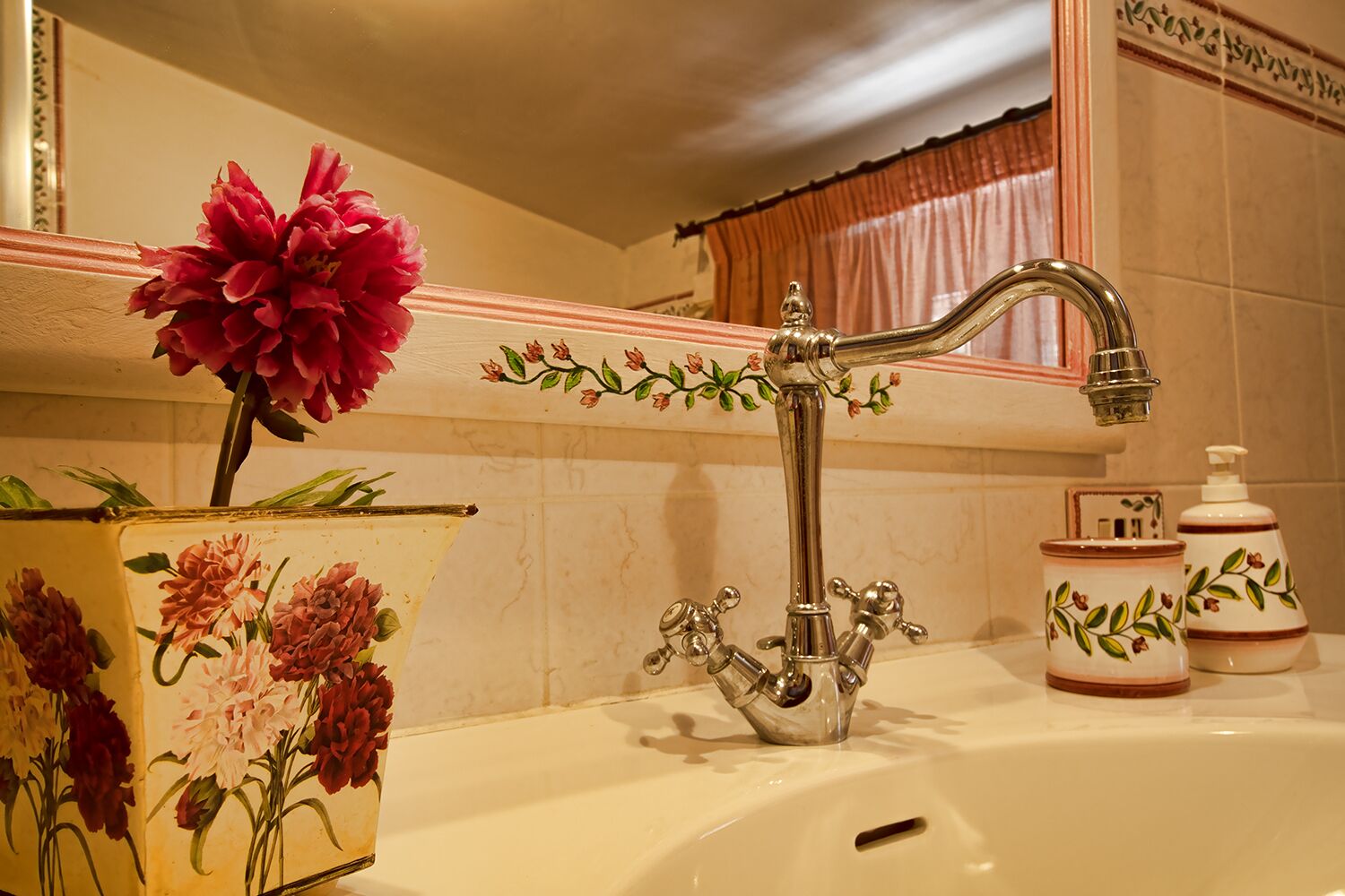 A bathroom with a classic design, featuring a decorative faucet, a vase with flowers, and toiletry items.