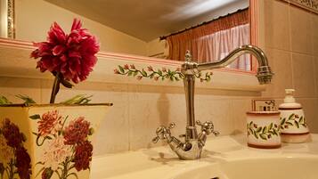 A bathroom with a classic design, featuring a decorative faucet, a vase with flowers, and toiletry items.