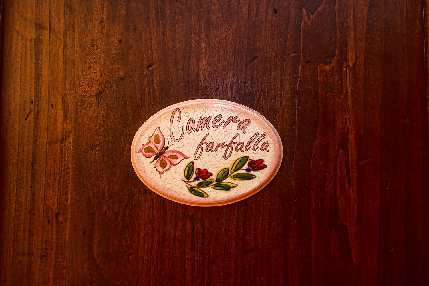 Superfície de madeira com uma placa oval decorativa exibindo o texto "Camera farfalla" e motivos florais.