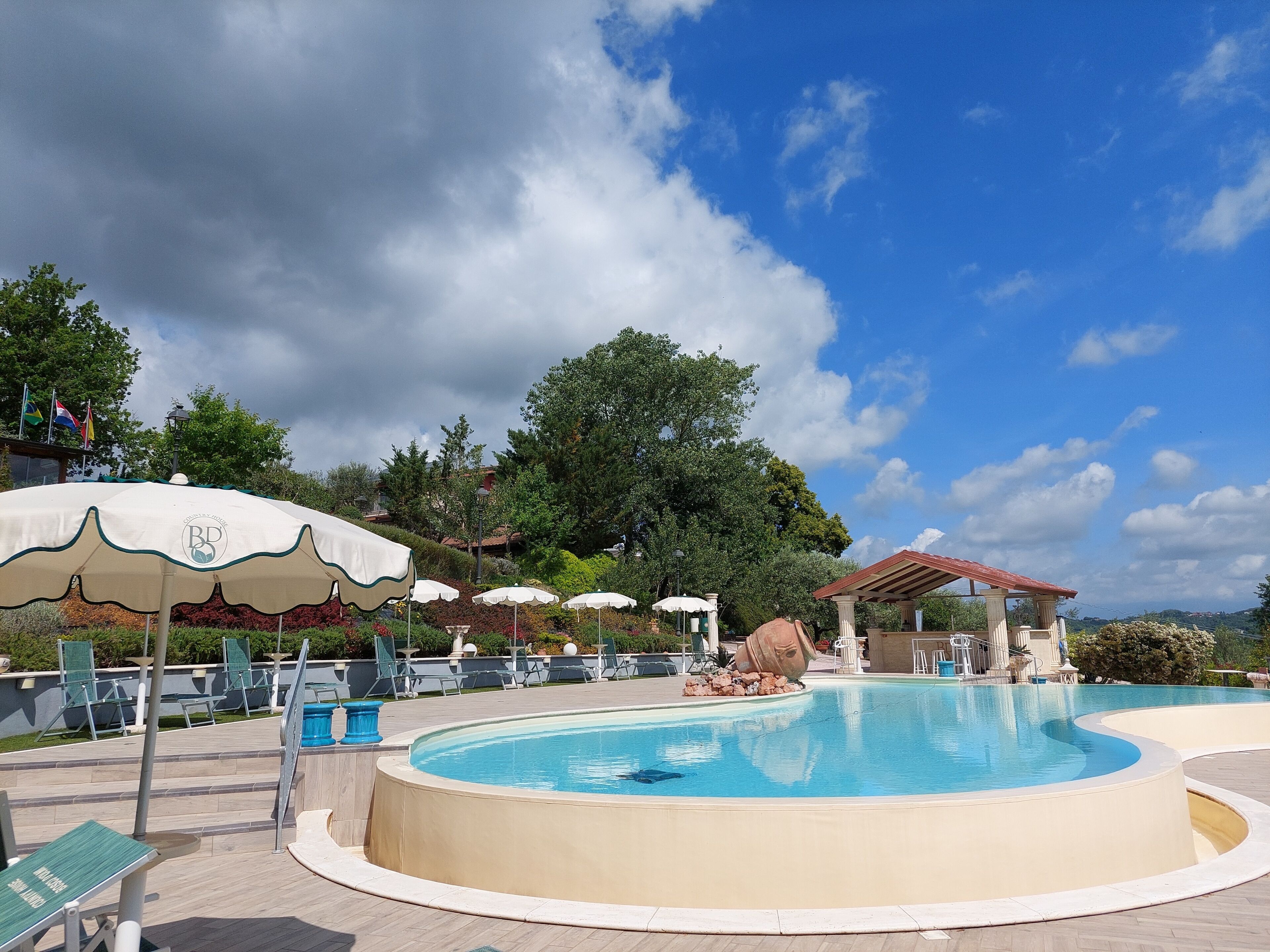 A swimming pool with lounge chairs and umbrellas, surrounded by trees and a clear sky.