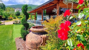 A wooden building with a covered patio, surrounded by lush greenery and a clear sky.