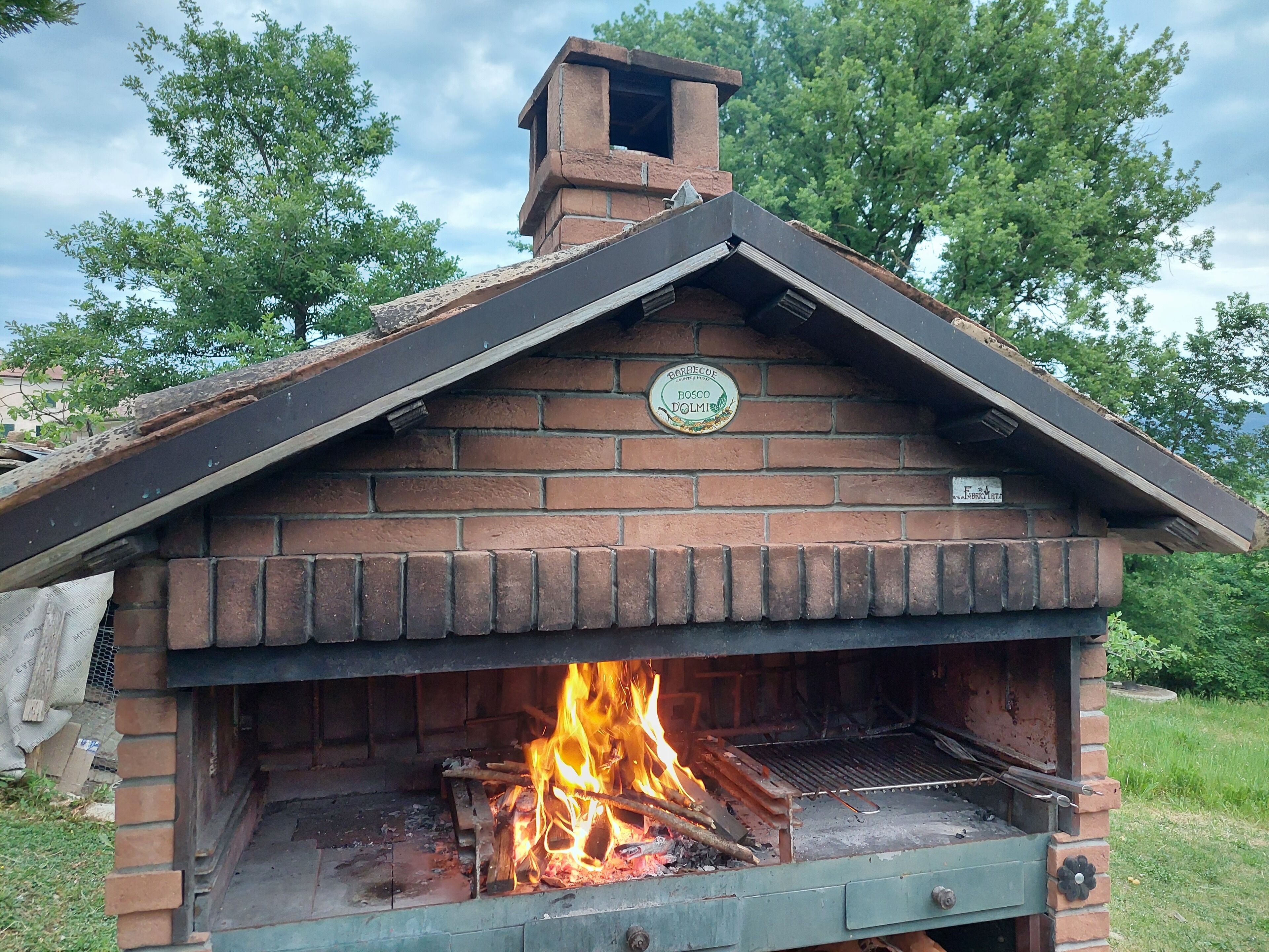 Ein gemauerter Außenofen mit Schornstein, in dem Feuer brennt, und ein Schild an der Wand.