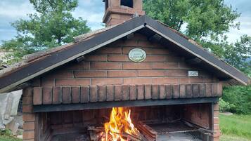 Ein gemauerter Außenofen mit Schornstein, in dem Feuer brennt, und ein Schild an der Wand.