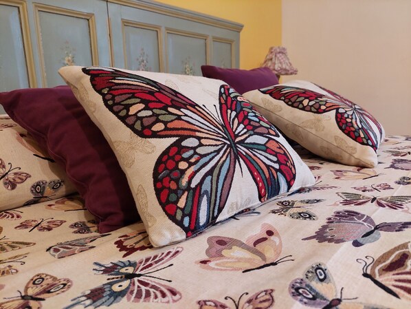 Een bed met een bloemenprintdeken en decoratieve kussens met vlinderdesigns.