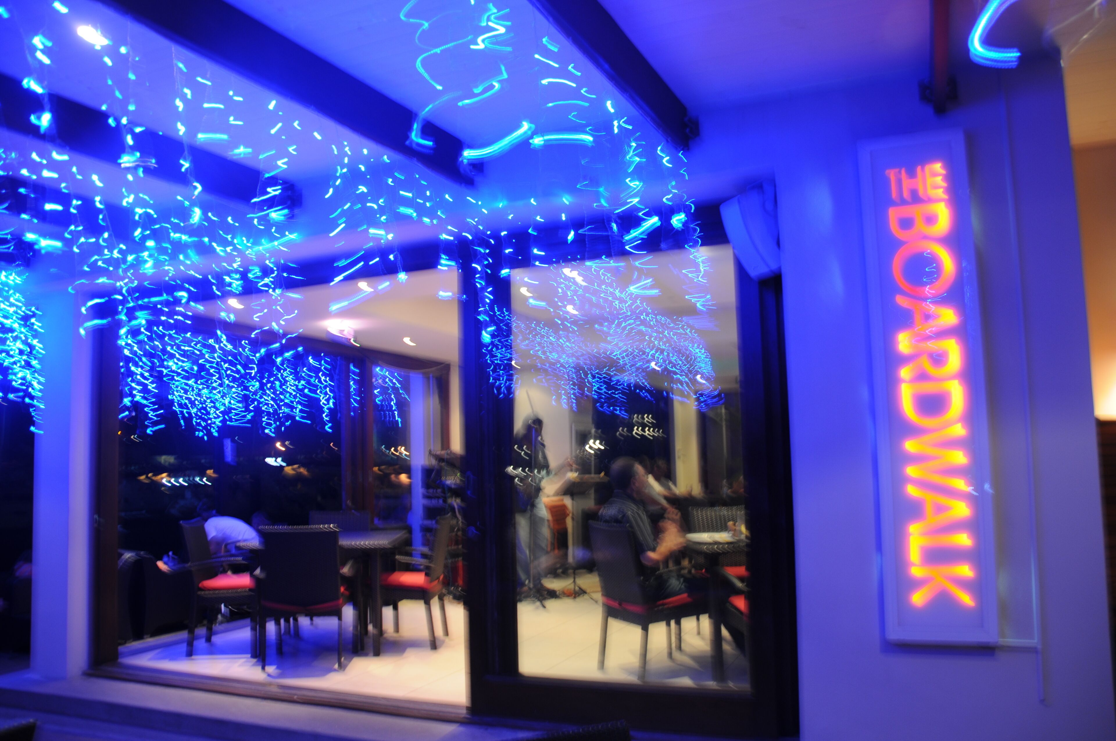 En restaurant med en neonskilte der siger "THE BOARDWALK" og blå lyskæder.