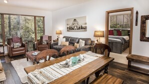 A cozy living room with a wooden dining table, leather sofas, and a large window with blinds. - Exclusive Arrowhead Village Condo, Steps from the Lift, garage, ski locker!! (Edwards)