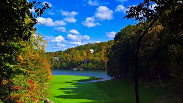 A golf course with a lake, surrounded by trees and houses.
