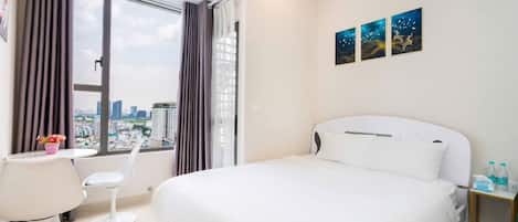 A hotel room with a large bed, a desk, two chairs, a window with curtains, and a city view.