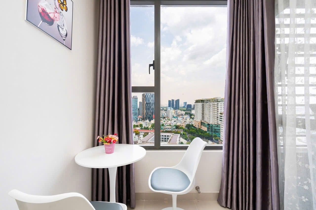 A room with a city view, a round table with a vase of flowers, and two chairs.