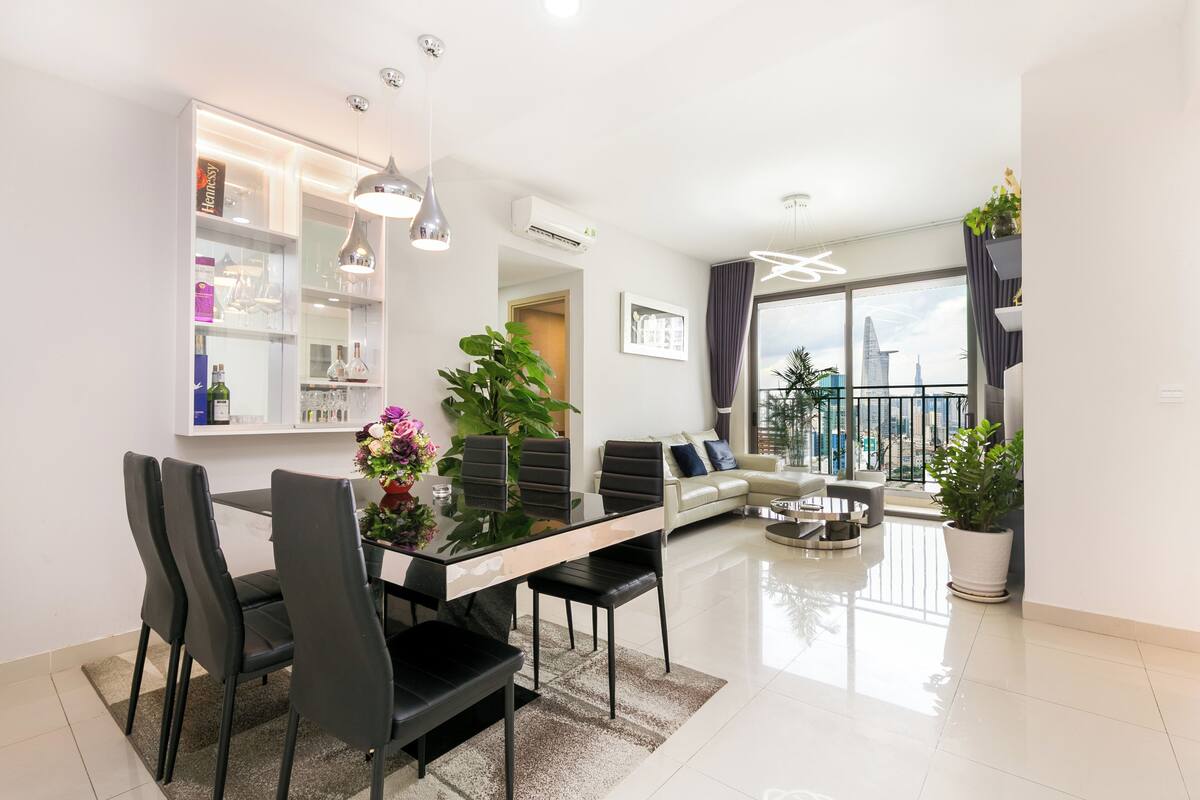 A modern living room with a dining area, a sofa, and a balcony with a city view.