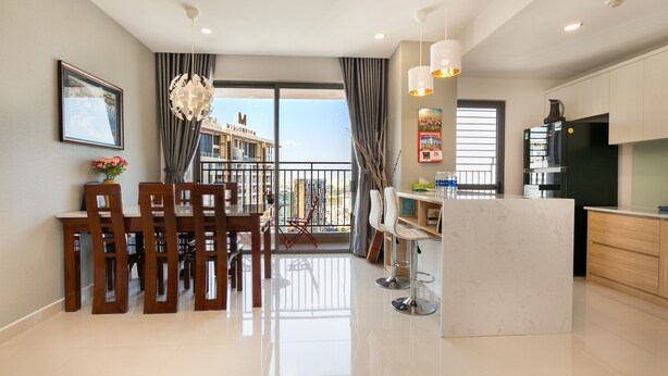 A modern kitchen with a black refrigerator, a dining area with wooden chairs, a white marble island, and a balcony with a view of buildings. - Trip Apartment Saigon (Ho Chi Minh City)