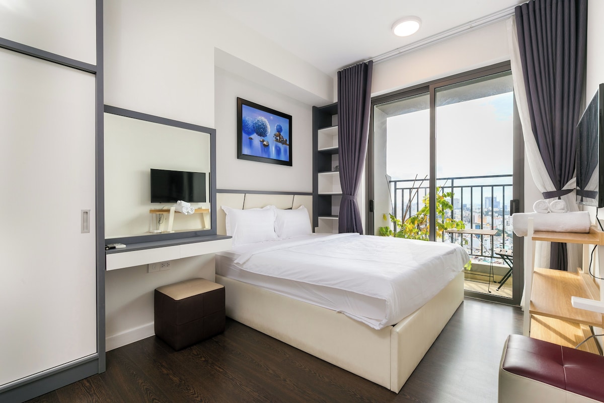 Une chambre d’hôtel moderne dotée d’un grand lit, d’une table de chevet, d’un miroir, d’une télévision et d’un balcon offrant une vue sur la ville.