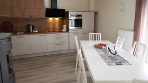 A modern kitchen with white cabinetry, a built-in oven, and a dining area with a white table and chairs. - Ferienhaus Victoria (Ilmenau)