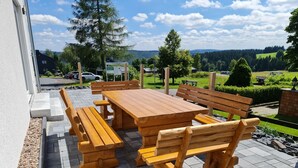 An outdoor patio with a wooden table and benches, surrounded by a stone pathway and greenery. - Ferienhaus Victoria (Ilmenau)