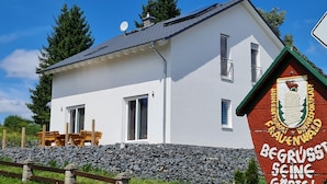 A white building with a sloped roof, a stone wall, and a wooden fence. - Ferienhaus Victoria (Ilmenau)