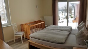 A room with a large bed, a wooden crib, a white chair, and a view of the outside. - Ferienhaus Victoria (Ilmenau)