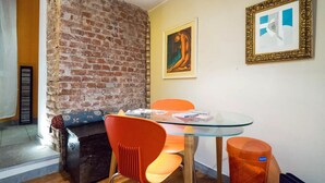 Comedor con mesa de vidrio, sillas naranjas, pared de ladrillo y una obra de arte enmarcada.