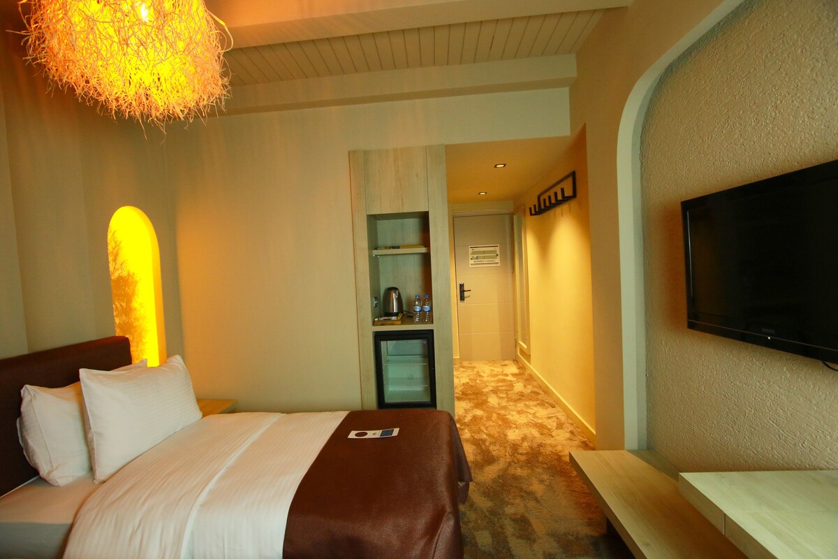 A hotel room with a bed, a television mounted on the wall, a small kitchenette, and a carpeted floor.