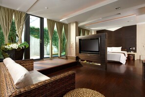 A modern hotel room with a large TV, comfortable seating, a bed, and a view of greenery. - Hofi Villa (Toucheng)