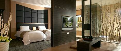 Une chambre d’hôtel moderne avec un grand lit, un téléviseur à écran plat fixé à un mur sombre, un coin salon avec une table basse et une vue sur un pont, visible par la fenêtre.