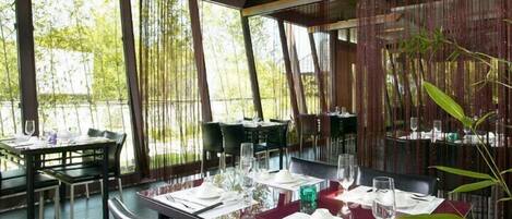 Un ristorante con tavoli apparecchiati, ampie finestre e decorazioni in bambù.