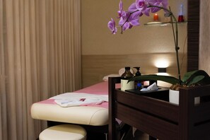 A massage table with a pink towel, a wooden side table with a potted plant, and a candle on a shelf. - Hofi Villa (Toucheng)