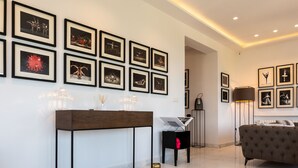 Ein modernes Wohnzimmer mit einer Couch, einem Couchtisch und einem Fernseher. An den Wänden hängen Bilderrahmen, und auf einem Beistelltisch steht eine Lampe.