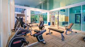 Een sportschool met diverse fitnessapparaten, waaronder loopbanden en gewichtstoestellen, en grote ramen met uitzicht op het omliggende landschap.