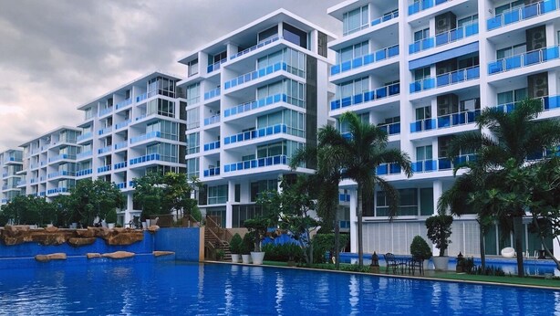 Een modern hotel met meerdere verdiepingen, een zwembad en palmbomen.