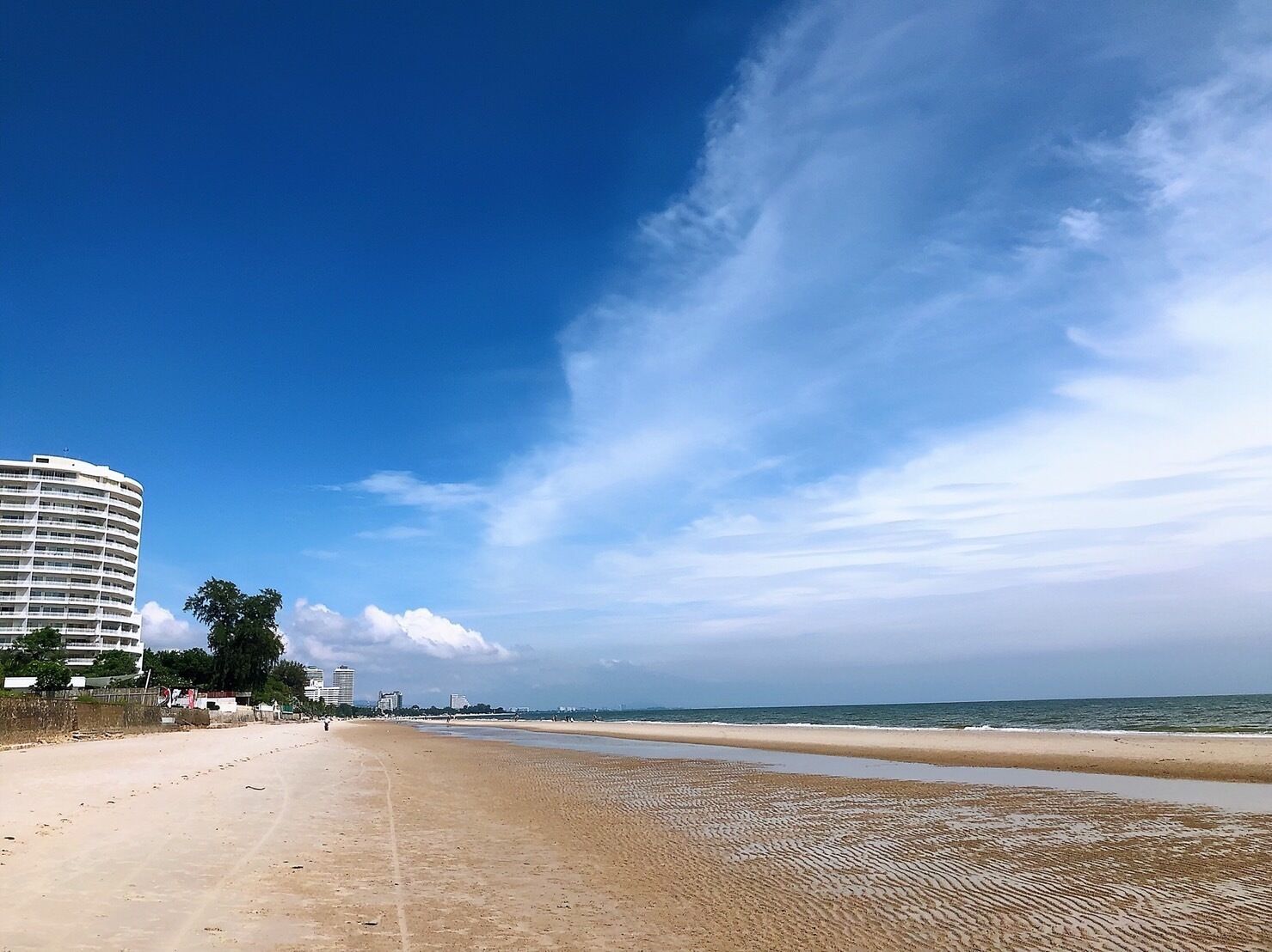 Ein Strand mit einem großen Hotelgebäude links, einem sandigen Ufer und dem Ozean im Hintergrund.