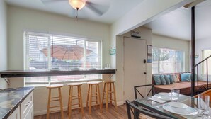 A kitchen with a bar stool seating area, a dining table with plates and glasses, and a ceiling fan. - Bring the whole family to this 4 bedroom beach house! (San Diego)