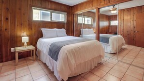 A wooden-paneled bedroom with two beds, a bedside table with a lamp, and a large mirror. - Bring the whole family to this 4 bedroom beach house! (San Diego)