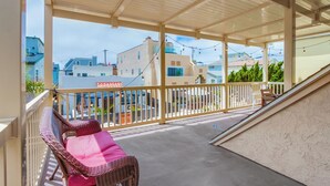 A covered balcony with wicker furniture and a view of surrounding buildings. - Bring the whole family to this 4 bedroom beach house! (San Diego)
