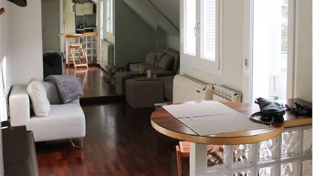 Un vaste espace de vie doté d’un haut plafond, d’un escalier menant à un niveau supérieur, d’une table à manger avec des chaises, et d’un coin salon confortable avec un canapé et des fauteuils.