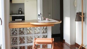 Une cuisine avec un plan de travail en bois, une bouilloire et une machine à café. Une porte donne accès à une autre pièce.