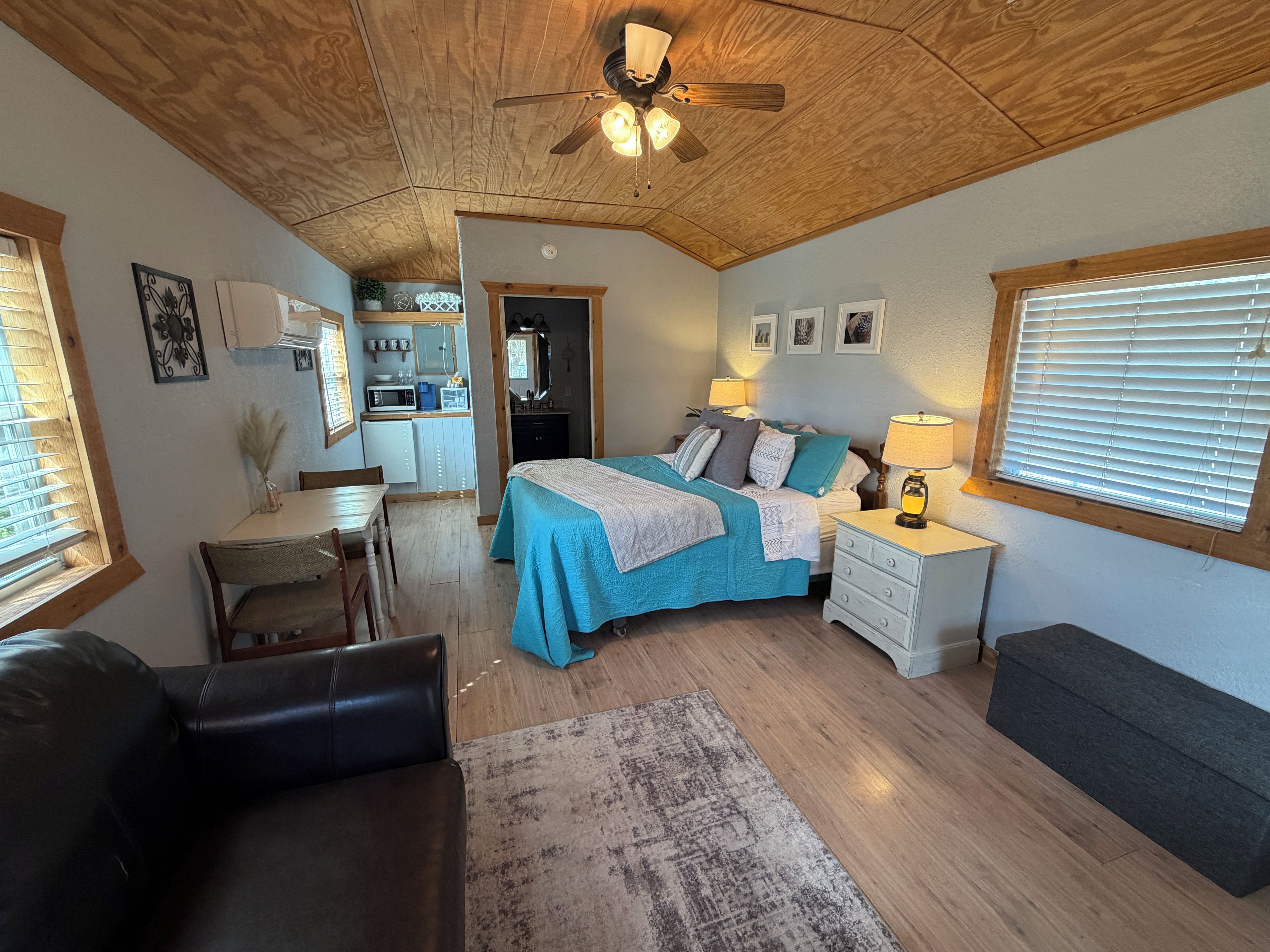 Un dormitorio con cama, mesitas de noche, escritorio y una kitchenette al fondo.