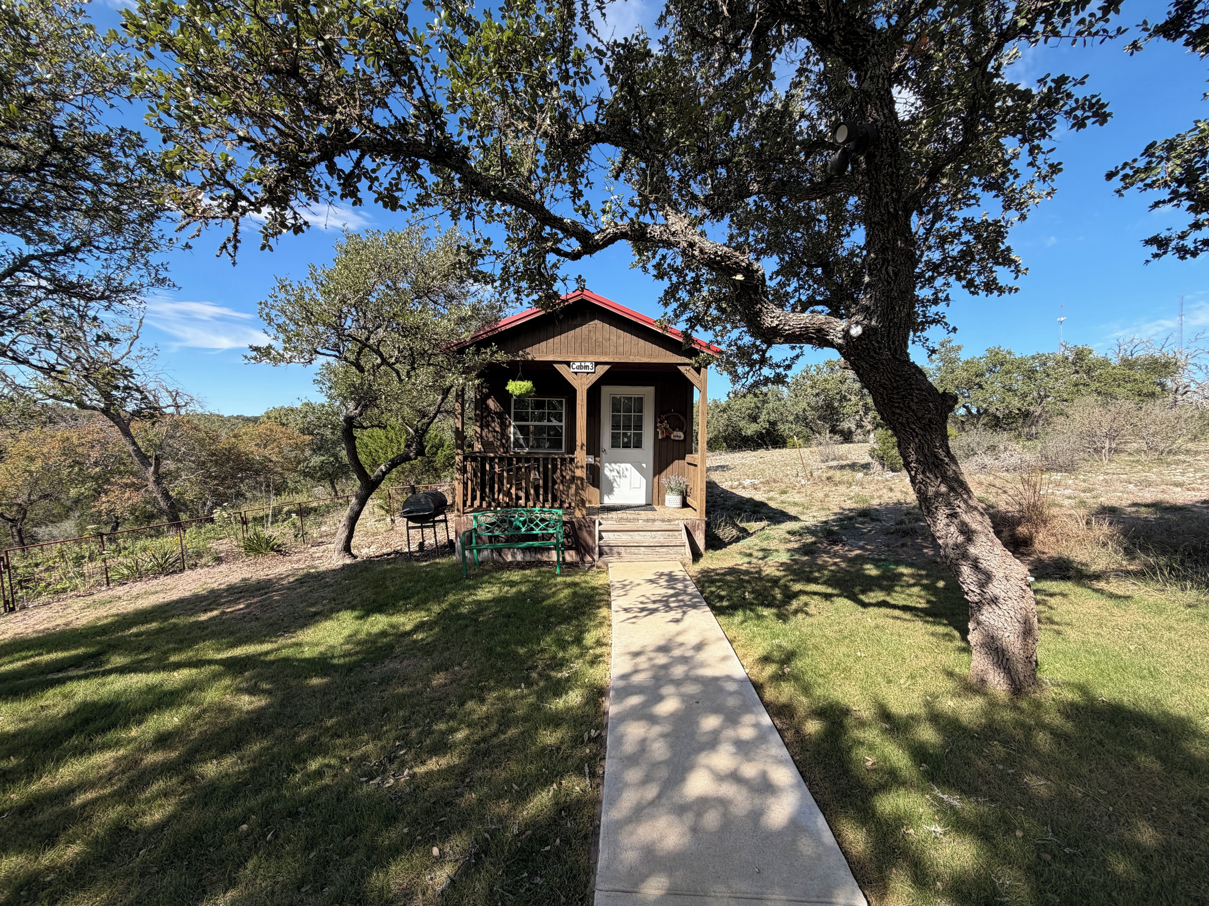 A wooden cabin with a red roof, a porch, and a pathway leading to it.