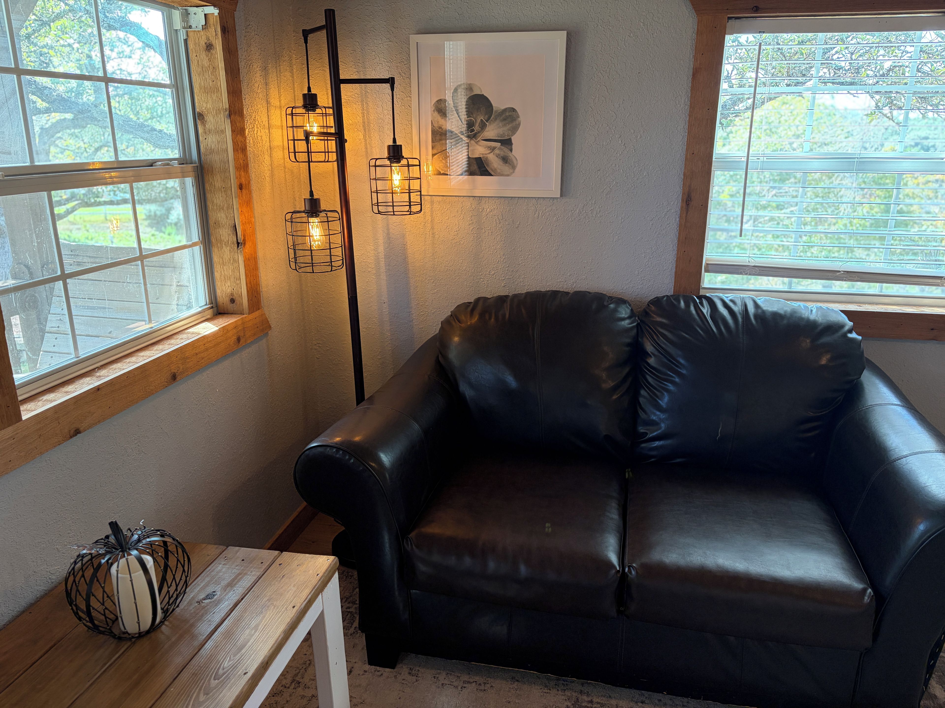 A room with a black leather sofa, a wooden table, a floor lamp, and a framed picture on the wall.