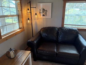 Ein Zimmer mit einer schwarzen Ledersofa, einem Holztisch, einer Stehlampe und einem gerahmten Bild an der Wand.