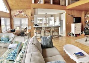 Ein geräumiger Wohnbereich mit einer Couch, Sesseln, einem Esstisch und einer Küchenzeile mit Fernseher und Kamin.