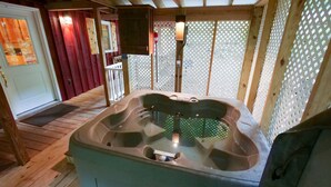 Ett bubbelbad i en stuga av trä, med en träveranda, en dörr och ett spaljéstaket.