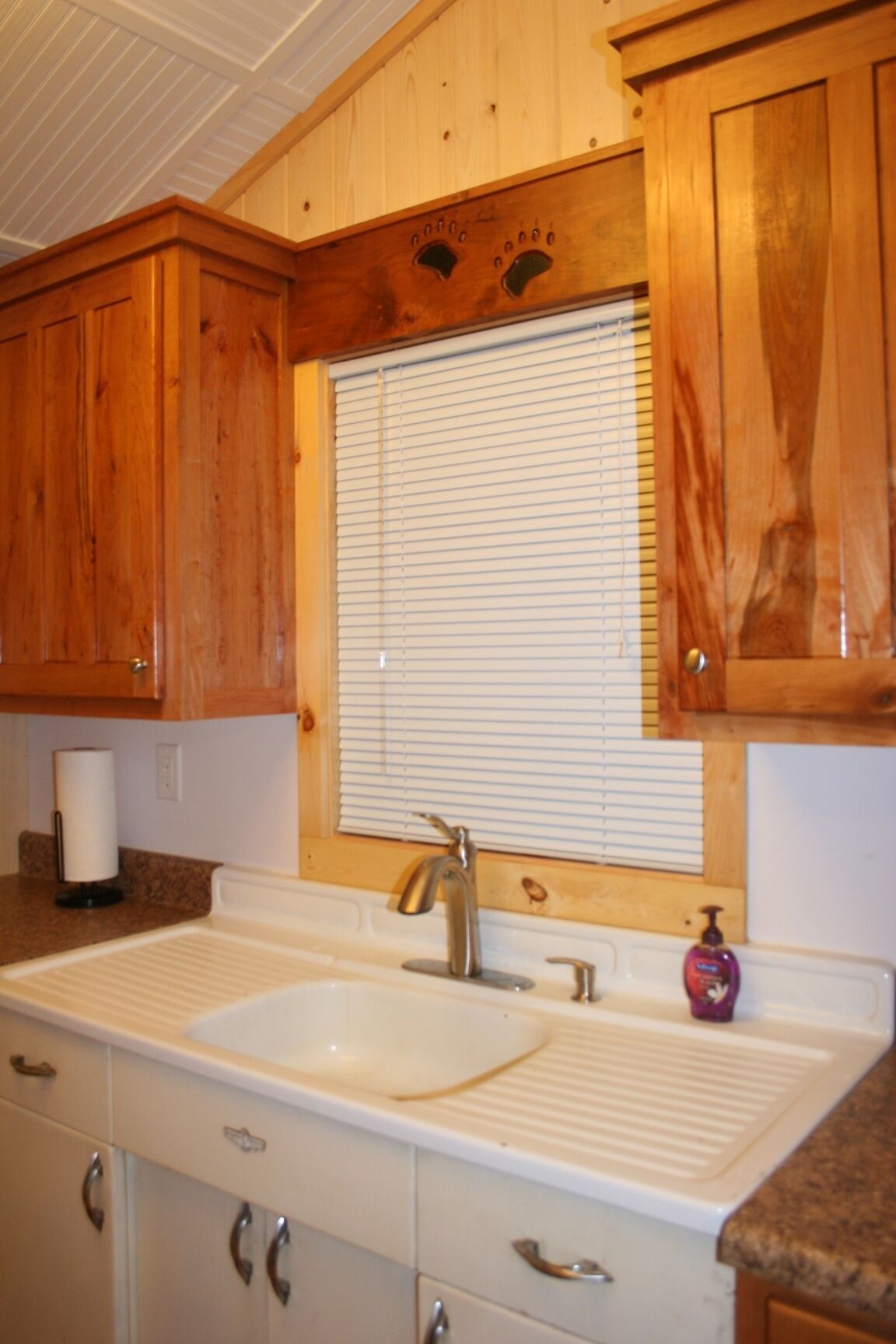 A kitchen with wooden cabinets, a white sink, and a window with blinds.