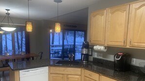 Una cocina con armarios de madera, lavavajillas empotrado, cafetera y comedor con mesa y sillas.