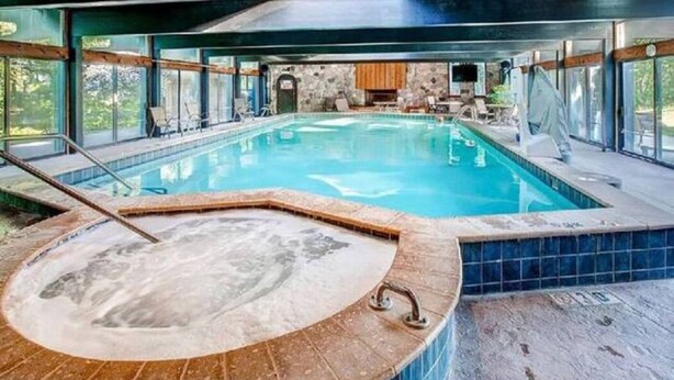 Una amplia piscina interior con jacuzzi, rodeada de paredes de piedra y grandes ventanales.