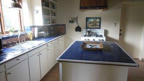 Una cucina con mobili bianchi, un piano di lavoro in piastrelle blu, un fornello e un lavello.