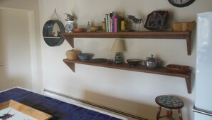 Una cucina con mensole in legno piene di utensili e libri, un orologio appeso al muro e un piccolo sgabello.