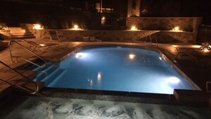 Une piscine avec un jacuzzi au fond, entourée de murs en pierre et dotée d’un éclairage extérieur.