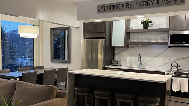 Une cuisine moderne dotée d’un îlot central, de tabourets de bar et d’un coin repas comprenant un canapé et des chaises.