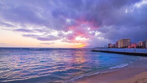 Een strand met een zonsondergang, een steiger en een stadsachtergrond.
