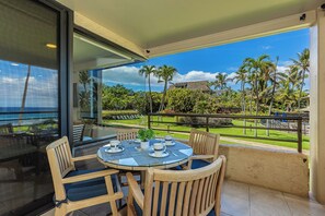 Ein Balkon mit rundem Tisch und Stühlen, der einen Blick auf einen tropischen Garten und den Ozean bietet.